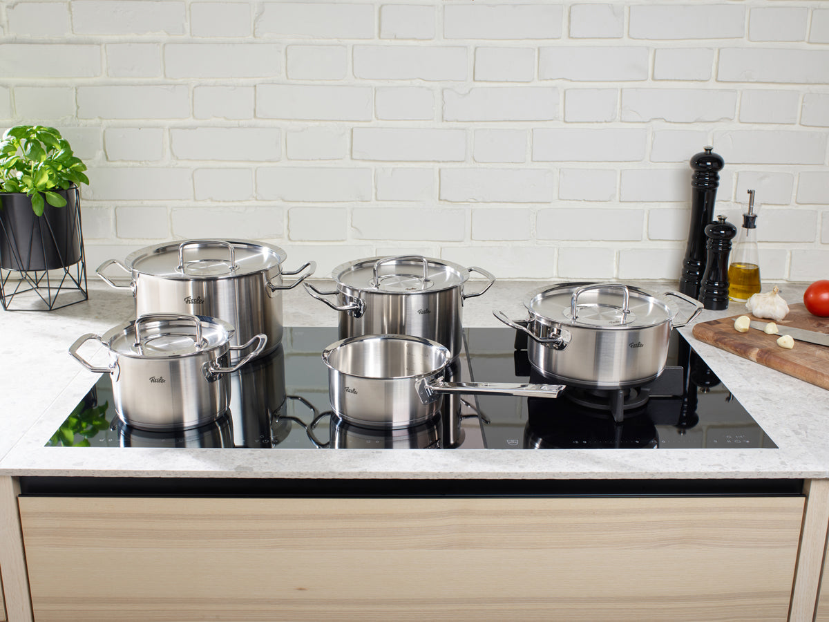 Fissler Original-Profi Collection® 5-piece stainless steel pot set with lids on stove, timeless design, German made, with vegetables and accents nearby.