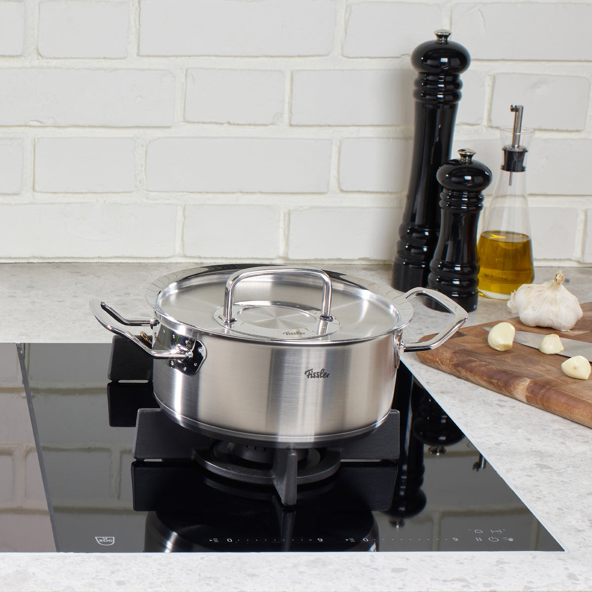 Original-Profi Collection® Casserole Pot by Fissler on gas stove, with Metal Lid. Induction suitable. Modern Kitchen Accessories in the background.