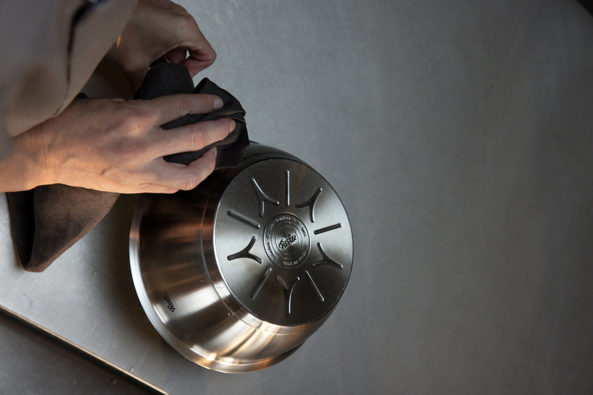Eine Person wischt die Unterseite einer Sauteuse (20 cm) aus der Fissler Original-Profi Collection® mit einem Tuch ab – ein Beispiel für Fisslers Tradition präziser Technik und langlebigen Designs.