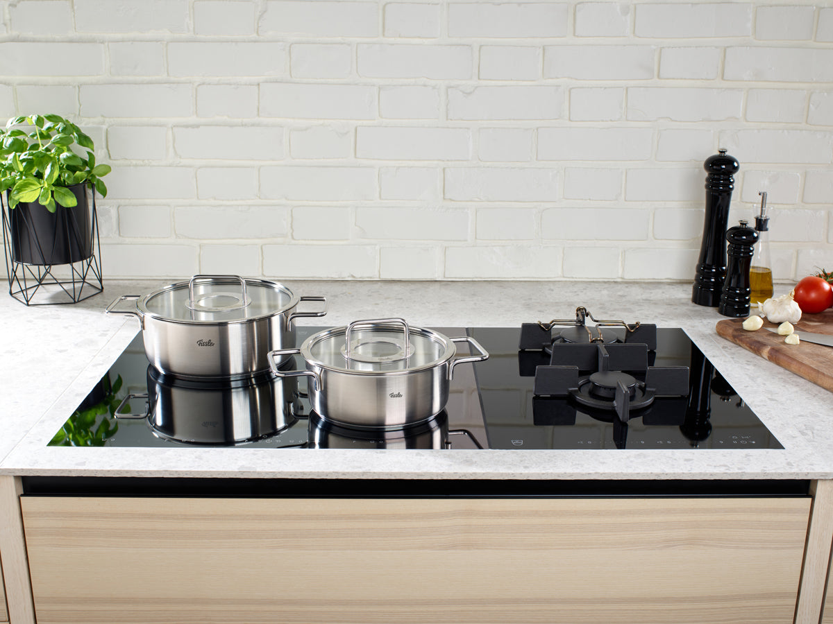A modern kitchen with the 4-piece Fissler Pure Collection® Cookware Set on a glass cooktop, with fresh ingredients and herbs nearby.