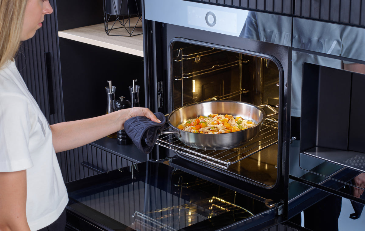 A person slides a Fissler Pure serving pan with vegetables into the oven; timeless German quality meets modern kitchen precision.