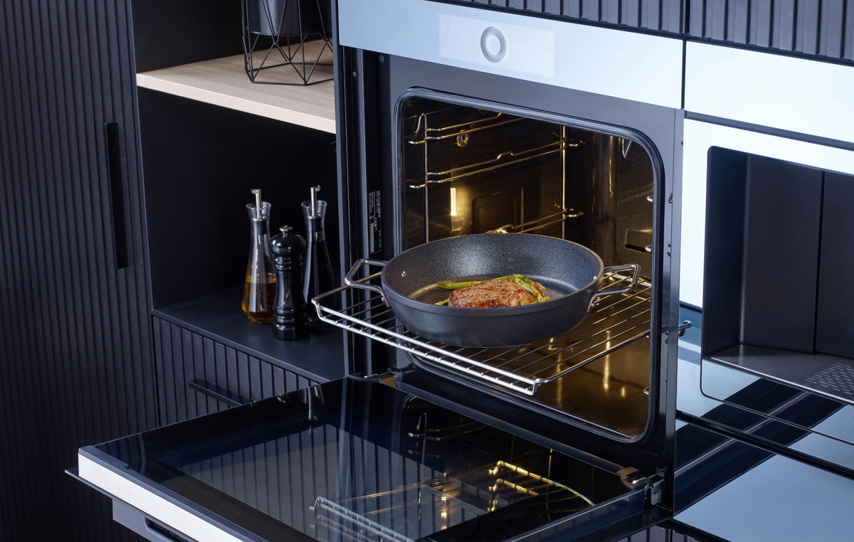 Ein Braten gart in einer Fissler Adamant® Servierpfanne - präzisionsgefertigt, antihaftbeschichtet, in einem offenen Ofen einer modernen deutschen Küche.