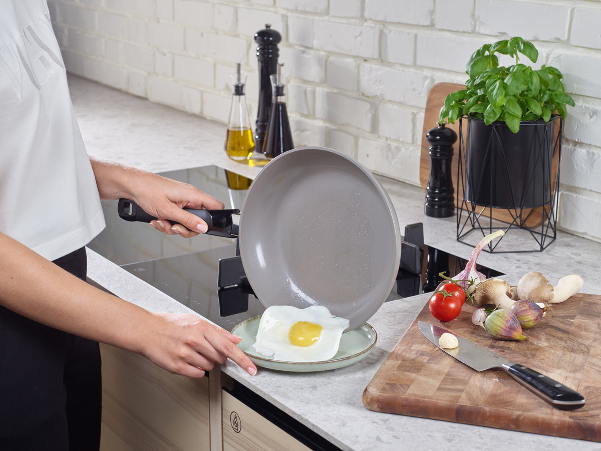 In a modern kitchen, a fried egg slides from the Fissler Ceratal® Classic Frying Pan Set onto a plate, with Fissler quality utensils beside it.