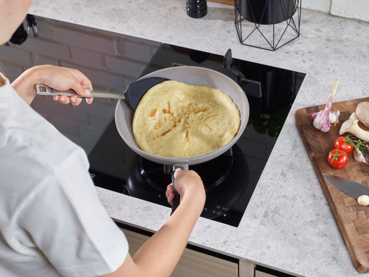 Preparing a crêpe in a Fissler Ceratal® Classic Frying Pan on the hob; fresh vegetables and mushrooms on the cutting board beside it.