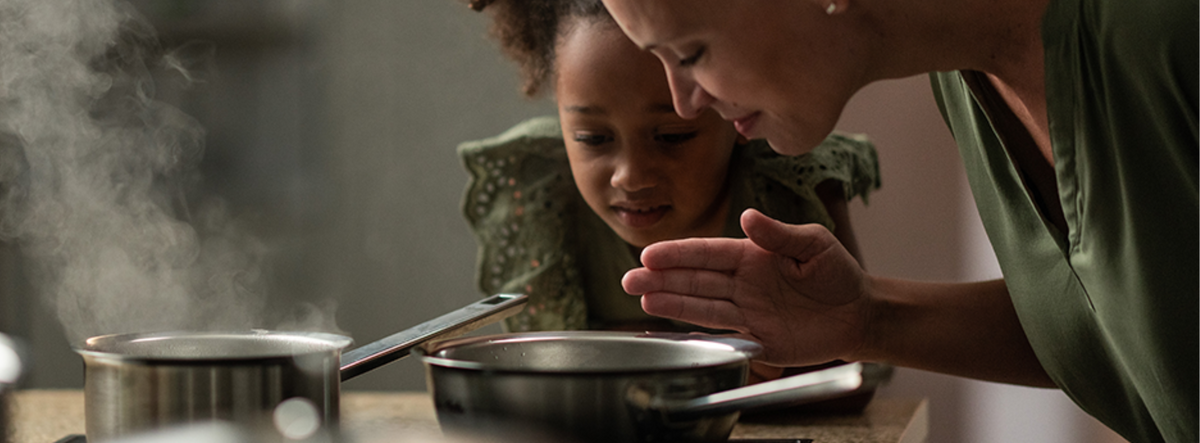 An adult and a child enjoy the aroma from a Fissler stainless steel pot, sharing a moment of curiosity and quality in the kitchen.