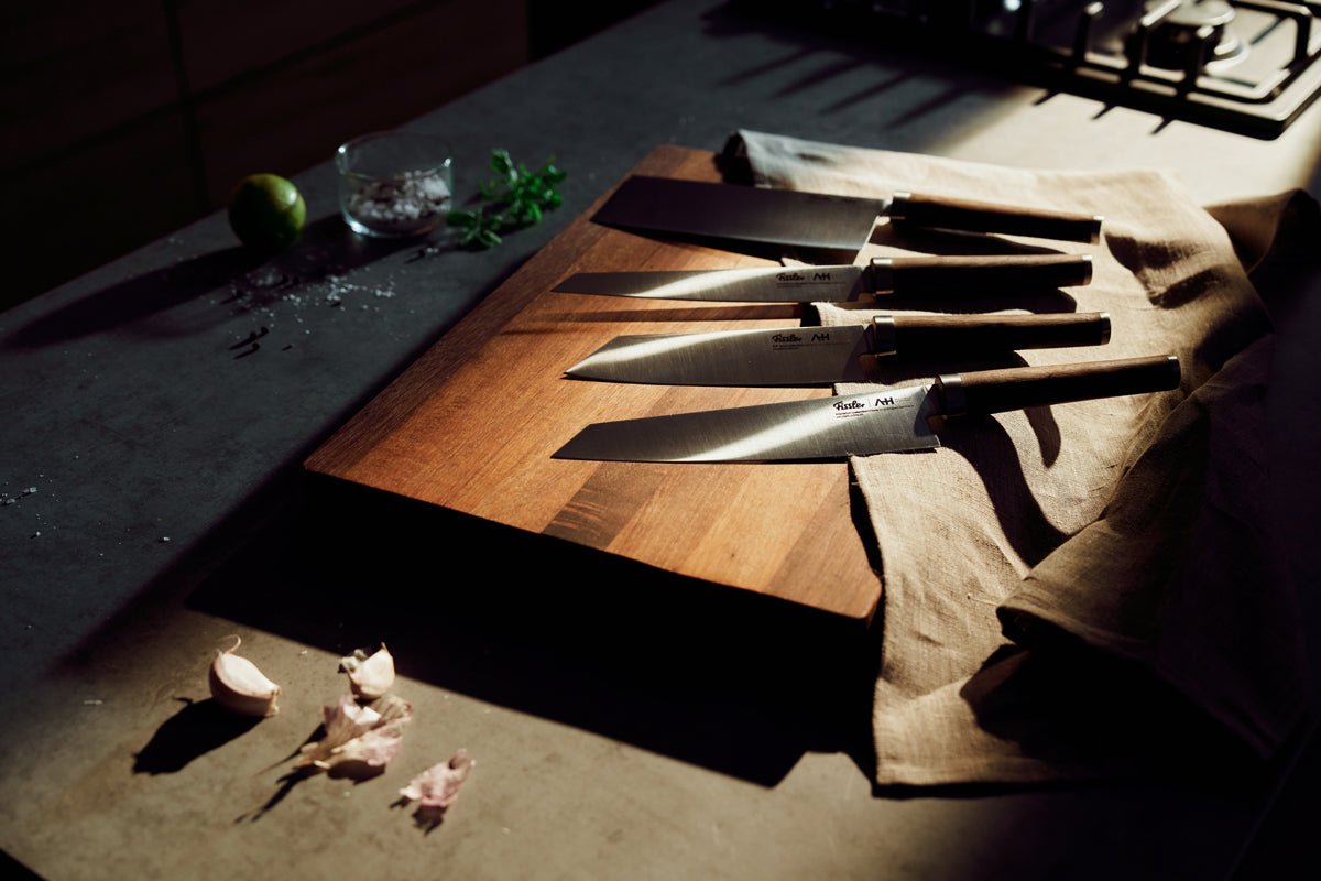 Das Fissler PrimeCut 18cm Chinesisches Kochmesser auf Holzbrett, graue Theke, mit frischen Zutaten - zeitlose deutsche Präzision.