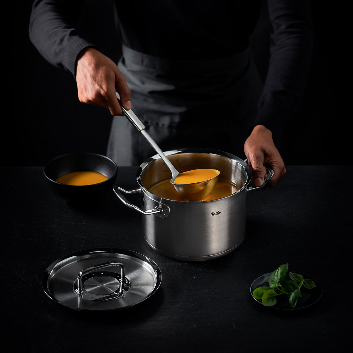 A person spoons soup with the Fissler Original-Profi Collection® soup ladle from a high-quality Fissler pot, radiating German precision.