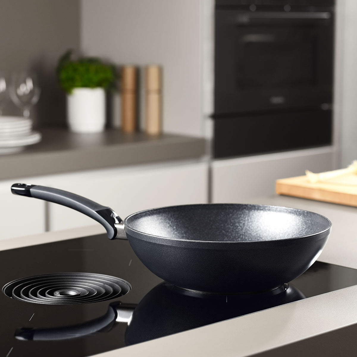 Fissler Adamant® Wokpfanne mit langlebiger Antihaftbeschichtung auf einem modernen Herd - zeitloses deutsches Design und Qualität für Ihre Küche.