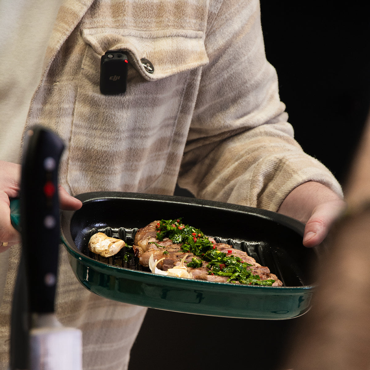 Eine Person hält eine Fissler Original-Profi Collection® Gusseisen-Grillpfanne mit Steak; modernes deutsches Design, Messer im Vordergrund.